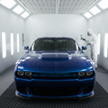 Car inside professional automotive paint booth with gleaming fresh metallic paint, painter with spray gun in background