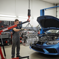 Used engine being lowered by engine hoist into car engine bay, mechanic guiding it, professional auto shop