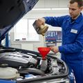 Professional mechanic pouring golden synthetic oil into car engine in auto service center