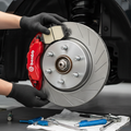 Front brake caliper and rotor with new ceramic brake pads being installed, red painted caliper