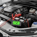 Digital battery tester with clamps on car battery showing green good reading