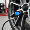 Digital tire pressure gauge on car tire valve stem with alloy wheel visible