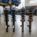 Two new shock absorbers next to two old rusty ones on shop floor with car lift in background